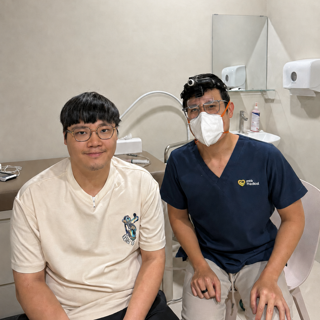 Dr Joel Foo seated beside a smiling male patient in the treatment room after his ear wax removal procedure at the Jurong clinic